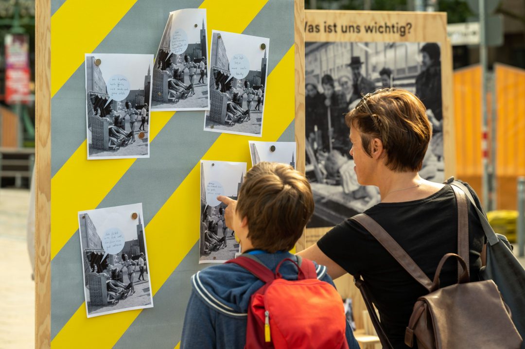 Partizipative Ausstellung im Stadtraum: Frau und Kind interagieren mit Fototafel des Projekts „Geschichte unterwegs“ in Hannover.