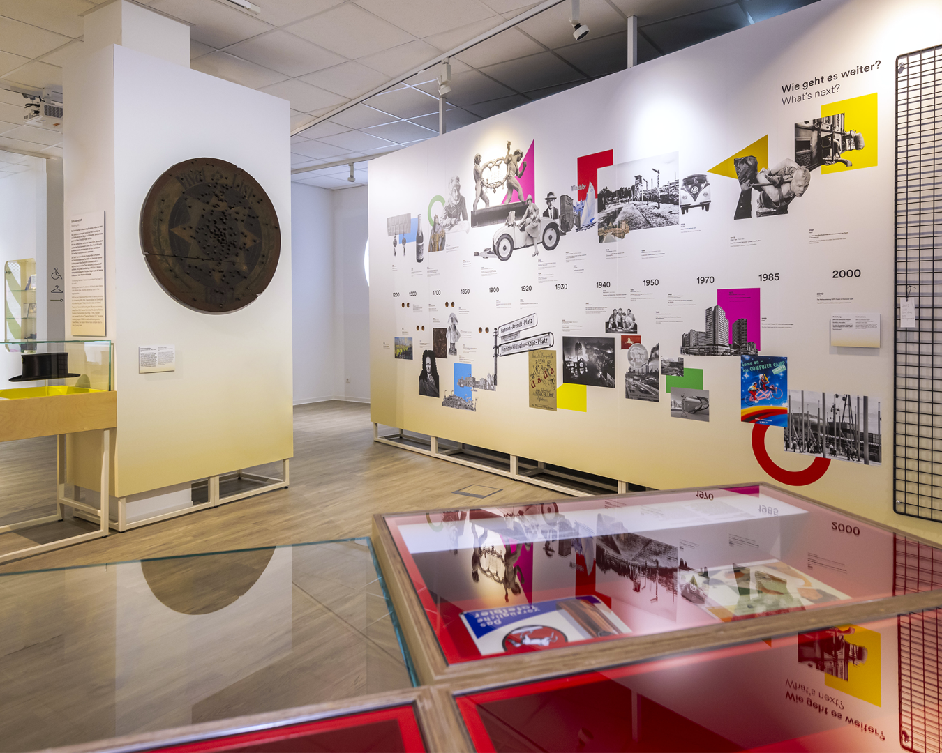 Innenansicht der Ausstellung im „Hannover Kiosk“: großer partizipativer Zeitstrahl, Vitrine im Vordergrund und einer Schützenscheibe links oben an einer Säule.