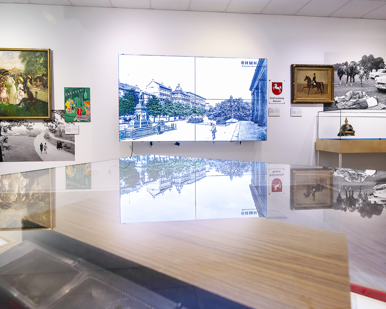 Innenansicht der Ausstellung im „Hannover Kiosk“: Historische Stadtansicht, Gemälde und Objekte wie Pickelhaube, kombiniert mit digitaler Präsentation.