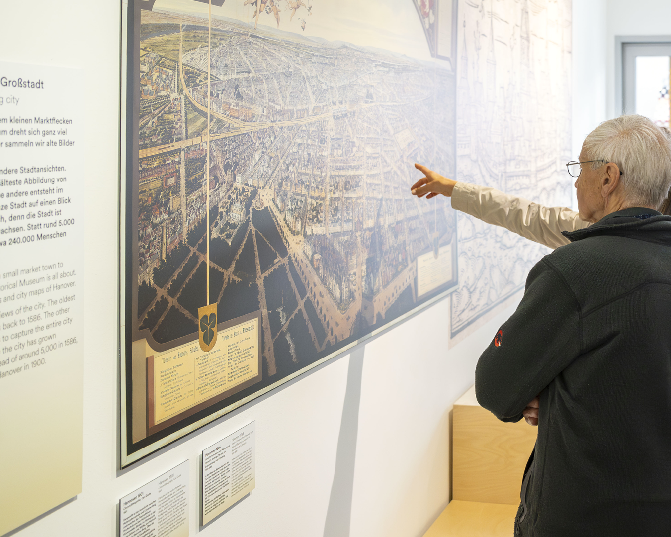 Innenansicht "Hannover Kiosk": zwei Menschen stehen vor einem historischen Stadtplan und zeigen darauf.