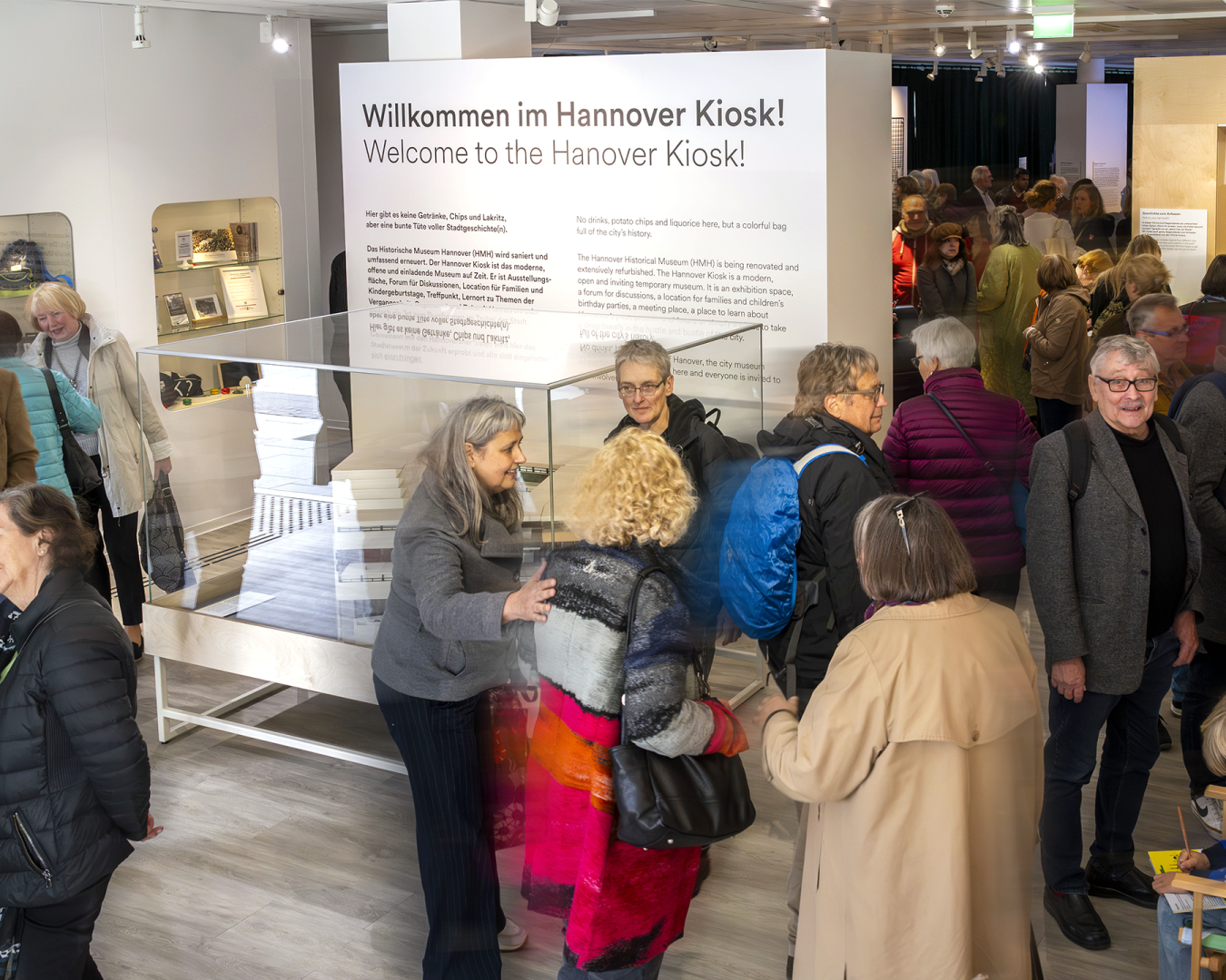 Eröffnung im „Hannover Kiosk“: Besucher_innen des Historischen Museums Hannover im Ausstellungsraum mit Begrüßungstext und Vitrine.