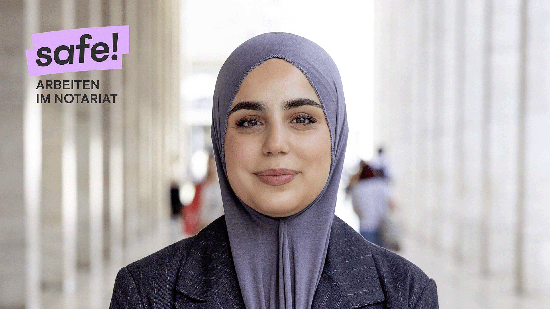 Eine Person im Anzug steht in einem Säulengang und schaut freundlich und selbstbewusst in die Kamera. Oben links steht das Kampagnenlogo safe! Arbeiten im Notariat