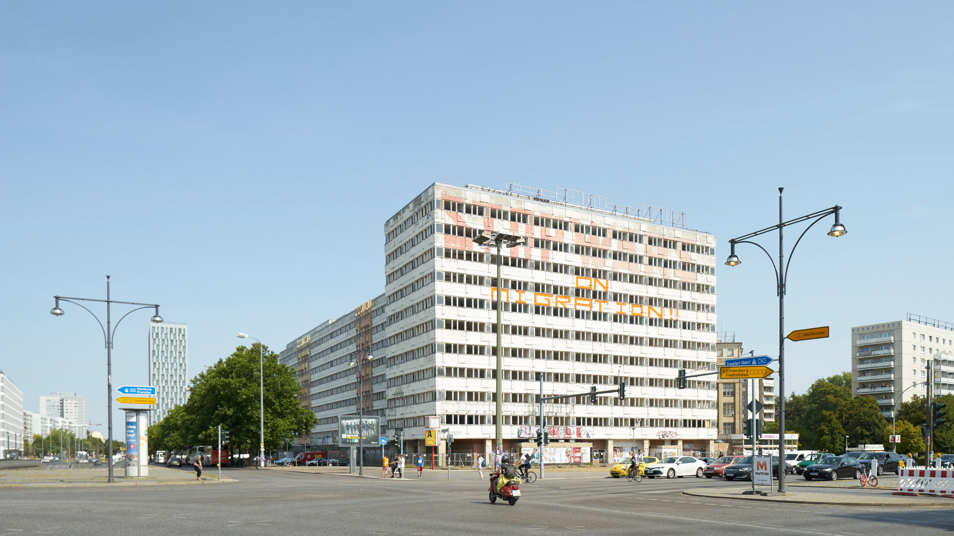 Blick über die Straßenkreuzung am Alexanderplatz in Berlin: Breite, mehrspurige Straßen. Im Hintergrund eine große vielstöckige Gebäudeanlage
