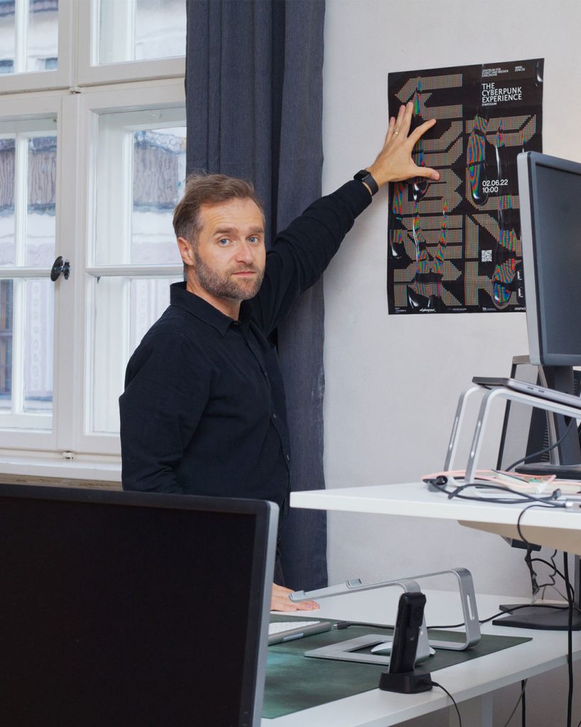 Eine Person steht vor einer Wand in einem Büro und hält ein schwarzes Poster fest