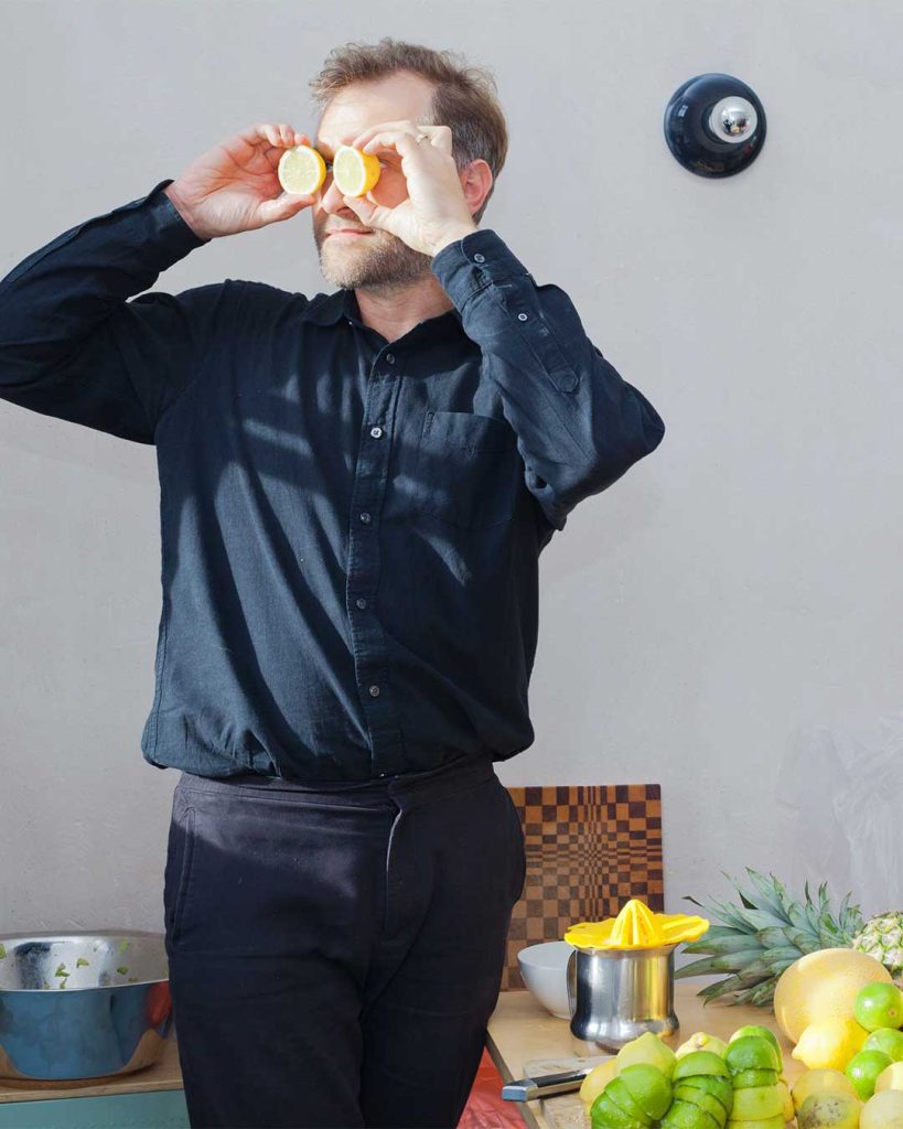 Eine Person hält sich Zitronen vor die Augen wie ein Fernglas. Schwarze Kleidung vor grauer Wand.