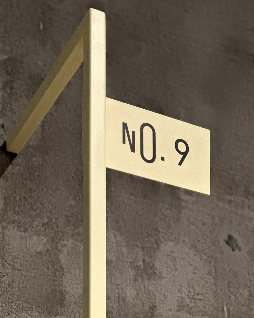 Gelber Winkel aus Stahl an Betonwand befestigt mit Schild, auf dem die Markierung „No. 9“ steht.