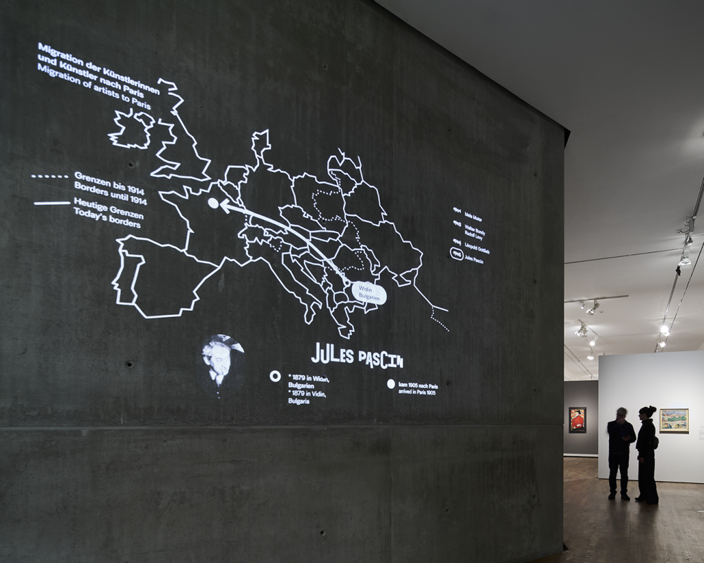 Projekttion einer Karte von Europa mit der Überschrift „Migration der Künstlerinnen und Künstler nach Paris“ mit einem Pfeil, der aus Sofia, Bulgarien, nach Paris zeigt. Darunter Kurzbiografie des Künstlers „Jules Pascin“