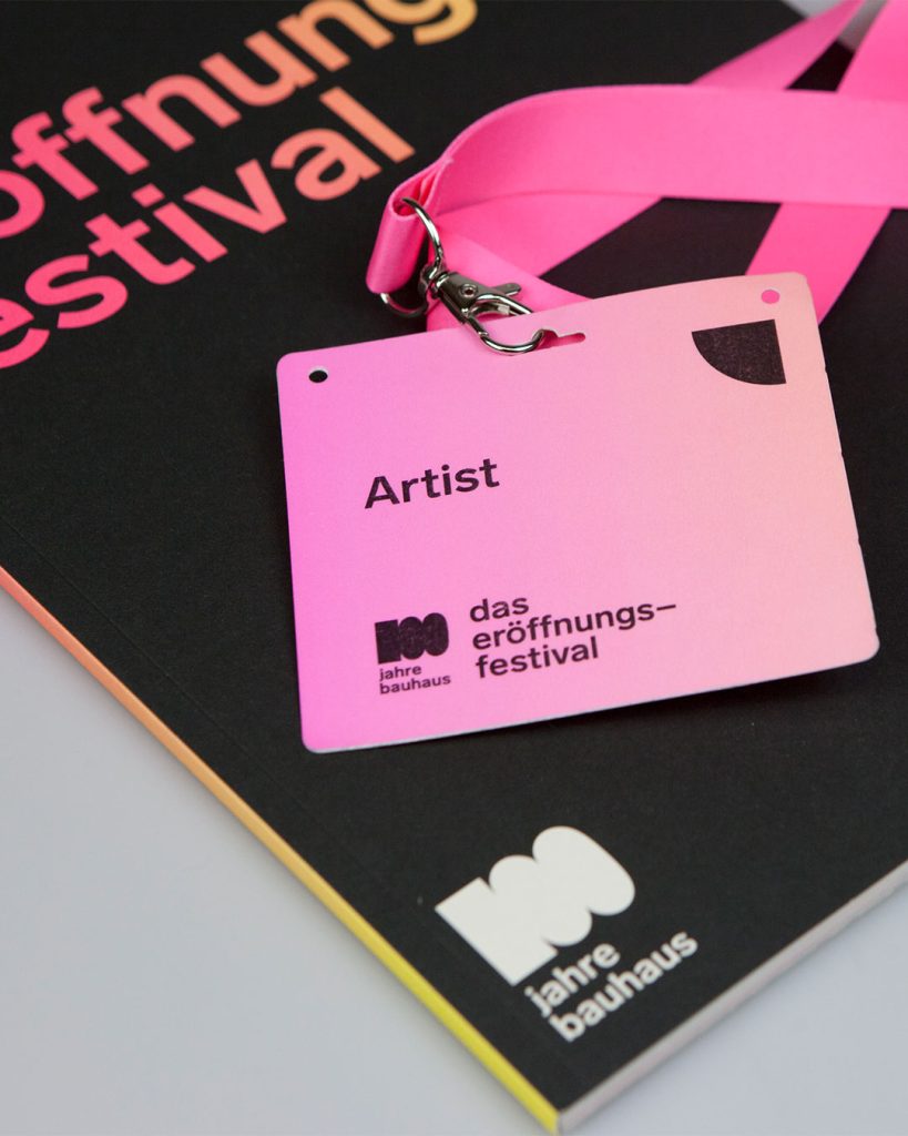 Pinker Badge mit Lanyard auf schwarzer Broschüre Veranstaltungsprogramm: 100 Jahre Bauhaus – 10 Tage Eröffnung. Das Festival.