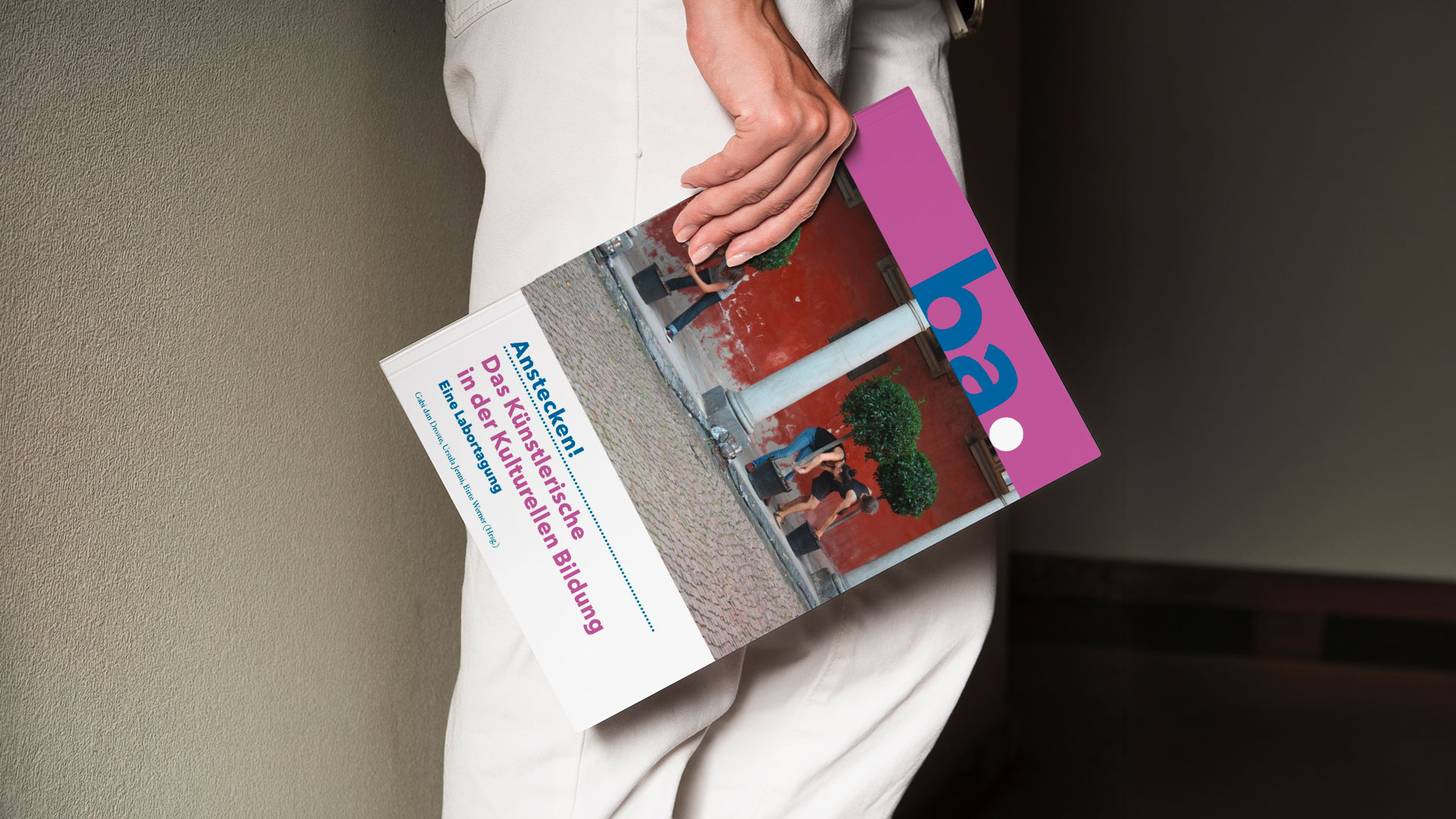 Seitliche Ansicht einer Person. Beinbereich. Person hält eine Publikation im Format DIN A4 mit dem Titel ba