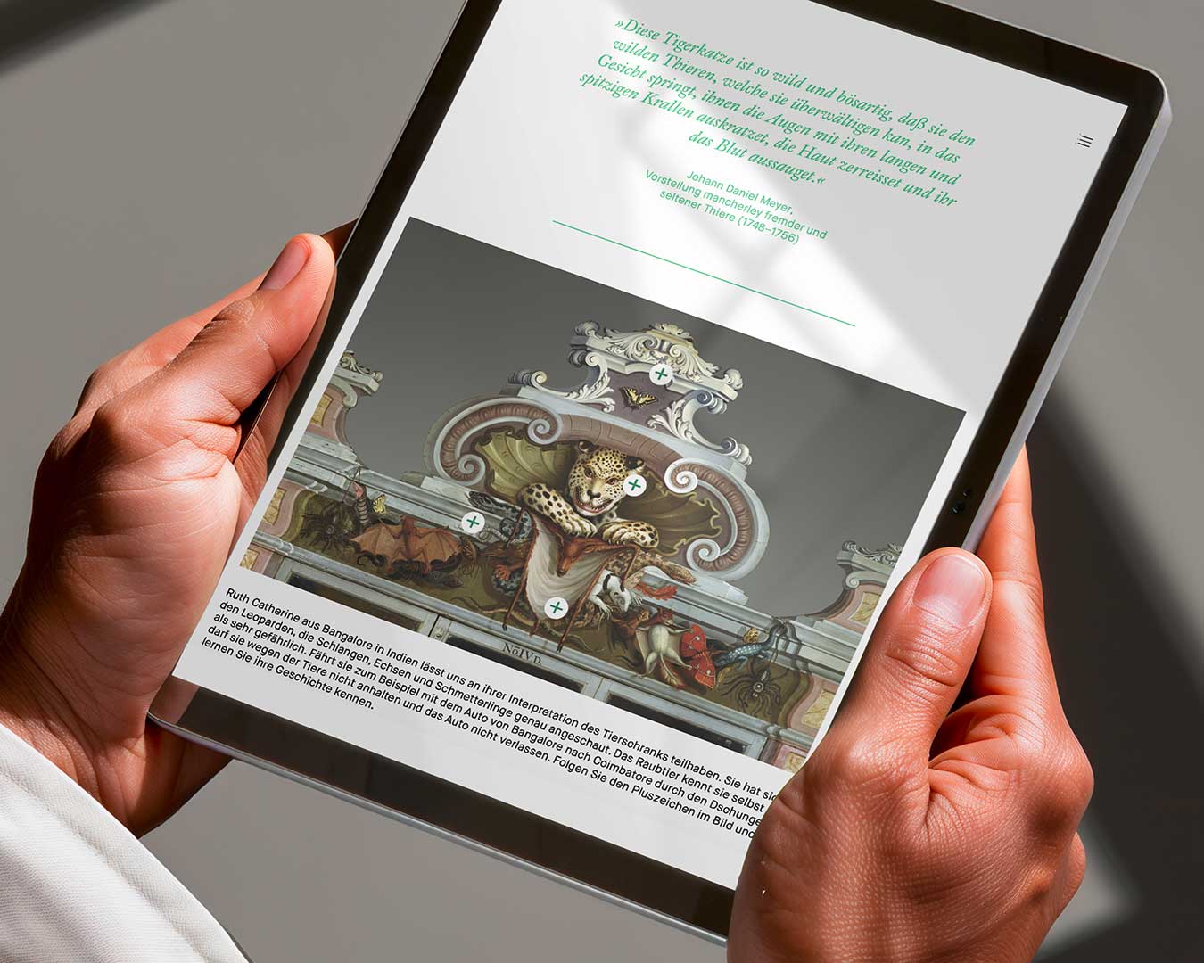 Eine Person hält ein Tablet mit der Ansicht einer Online-Ausstellung. Blick über die Schulter.