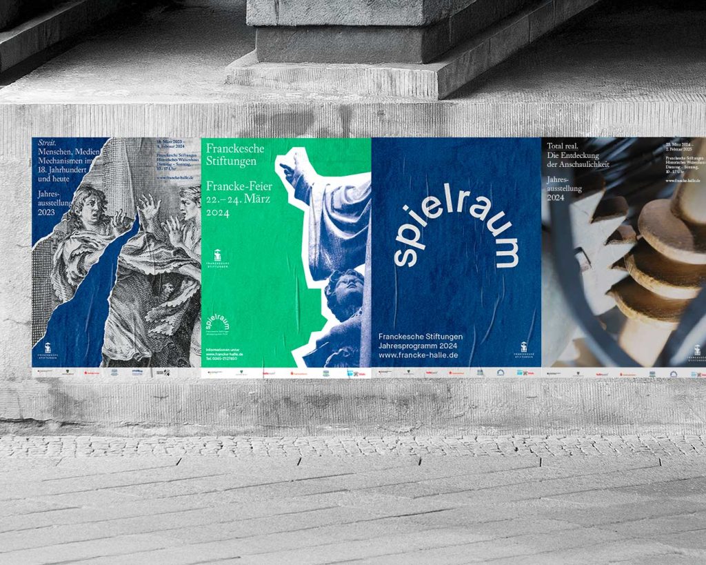 Plakate von Veranstaltungen der Franckeschen Stiftungen auf der Wand eines Brückenpfeilers. Streit, Francke Feier, spielraum und Total real – die Entdeckung der Anschaulichkeit. Weiße Schrift auf blauen und grünen Motiven.