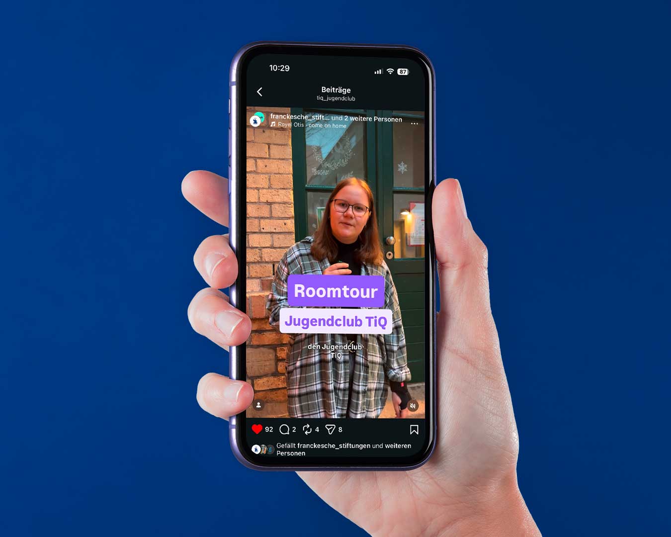 Social Media Kanal der Franckeschen Stiftungen. Eine Hand hält ein Smartphone. Roomtour Jugendclub TiQ. Eine Person mit Mikrofin steht vor einem Gebäude-Eingang.