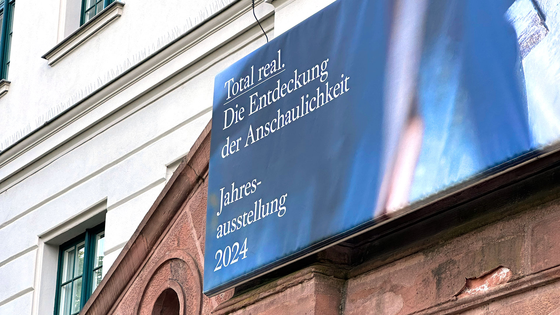 Fassade des Waisenhaus der FRanckeschen Stiftungen in Schränansicht mit Banner „Total real. Die Entdeckung der Anschaulichkeit – Jahresausstellung 2024“
