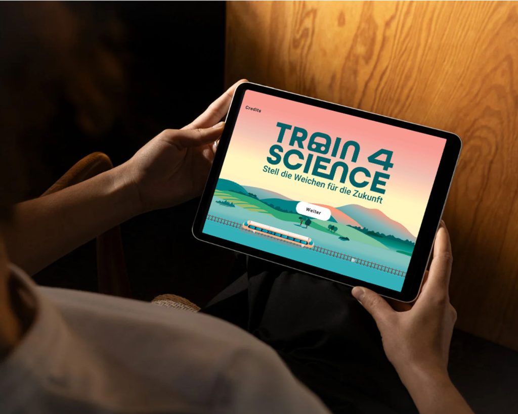 Blick von oben über die Schulter einer Person auf ein Tablet Display mit der Game-App „Train for Science“