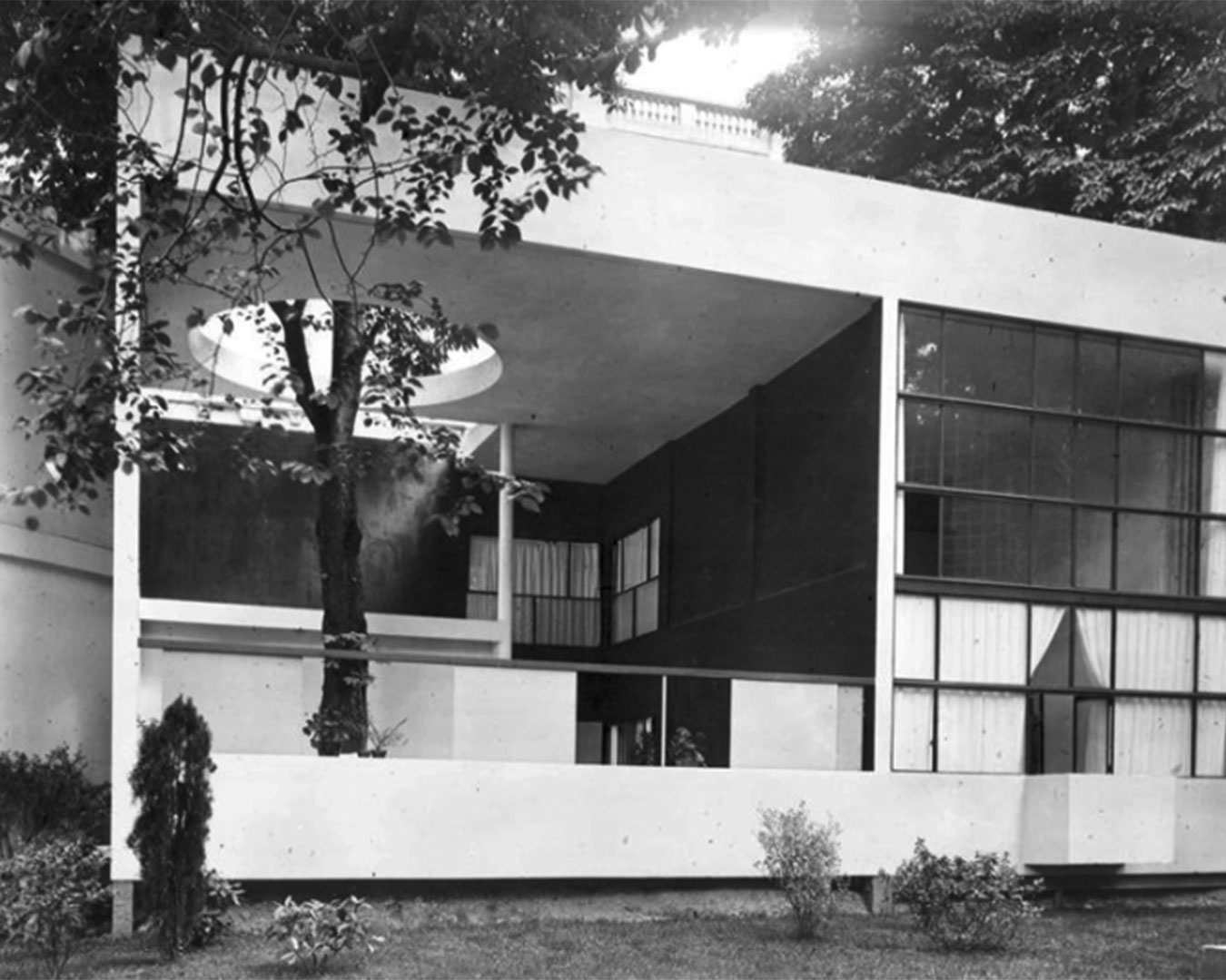 Historische Fotografie mit offener Gebäudearchitektur. Aus einer Einbuchtung wächst ein Baum durch eine Öffnung im Obergeschoss.