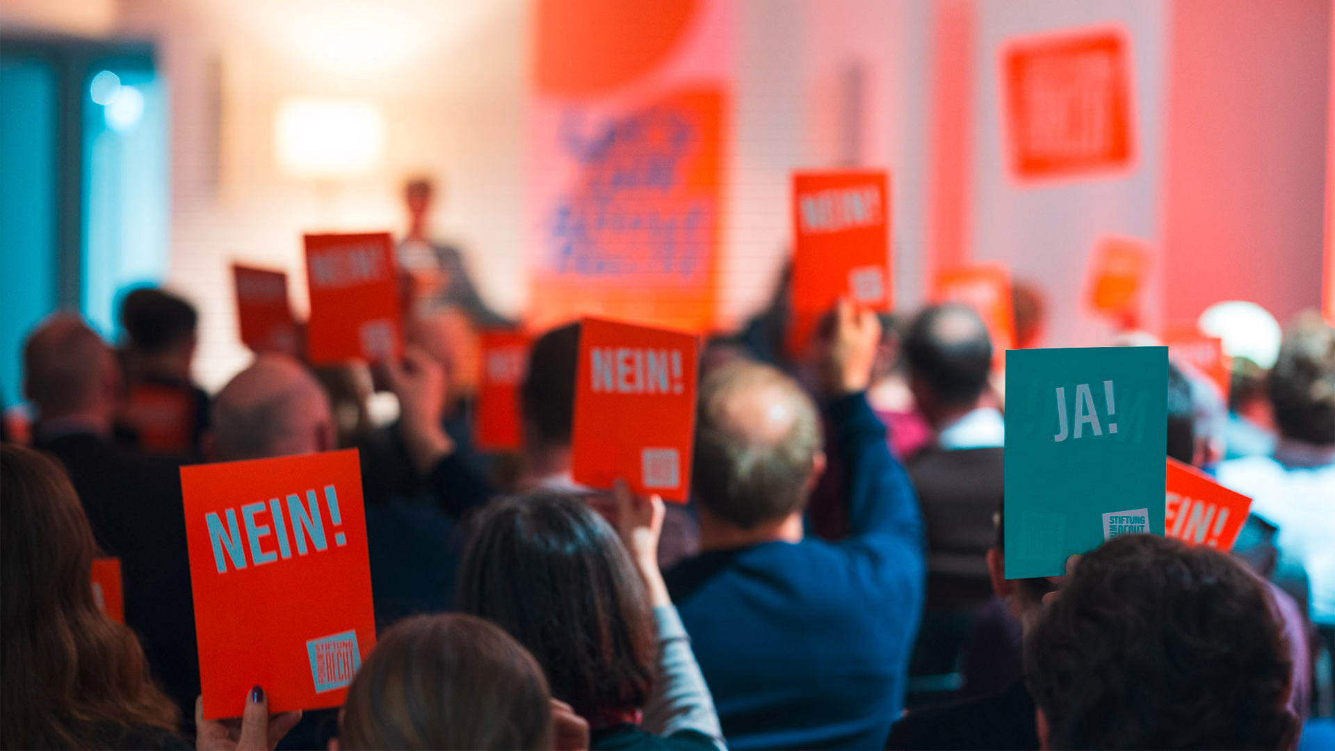 Blick von hinten über Publikum hinweg. erhobene Karten mit JA! und NEIN! Aufschrift.