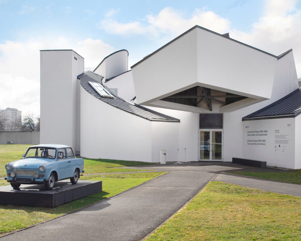 Blick auf ein weißes Museumsgebäude in moderner Architektur. Davor ein Trabbi.