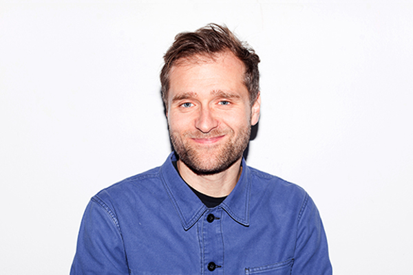 Portrait von Rik Watkinson, dunkelblonde Person mit blauem Hemd und schwarzen Knöpfen