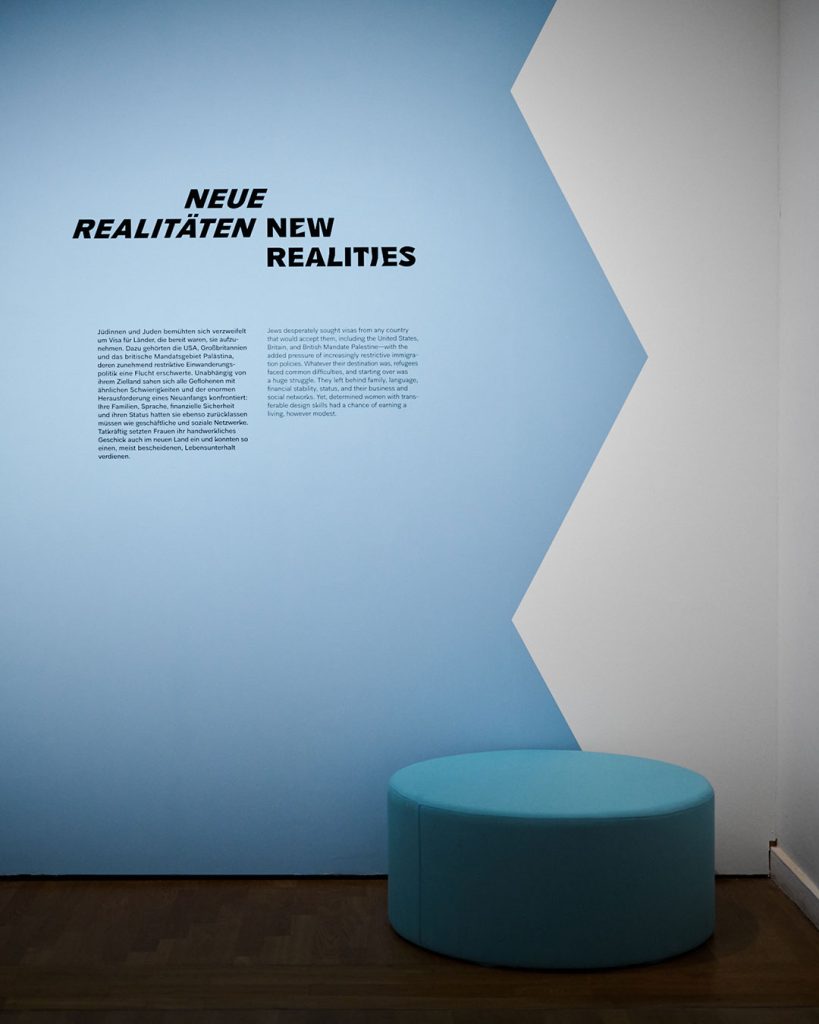 Raumansicht Ausstellung Widerstände. Wand mit Sitzmöbel in Hellblau. Wandtext: Neue Realitäten