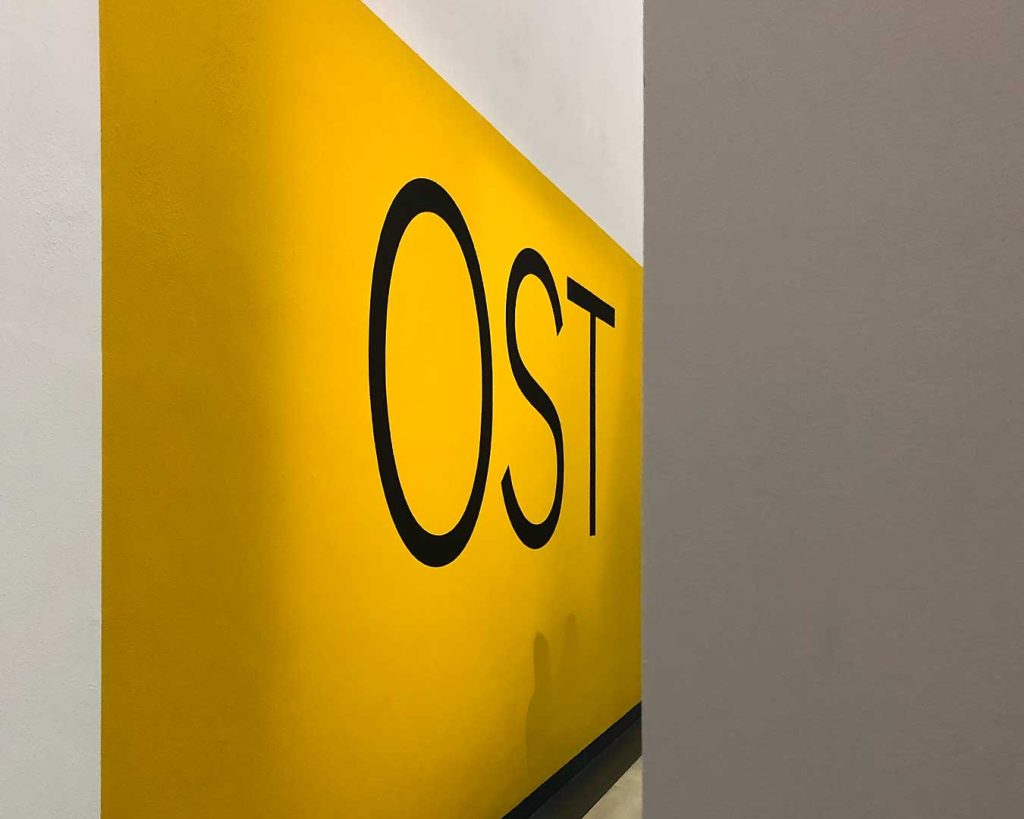 Gelbe Wand mit dem Wort „OST“ in Ausstellungsaufbau