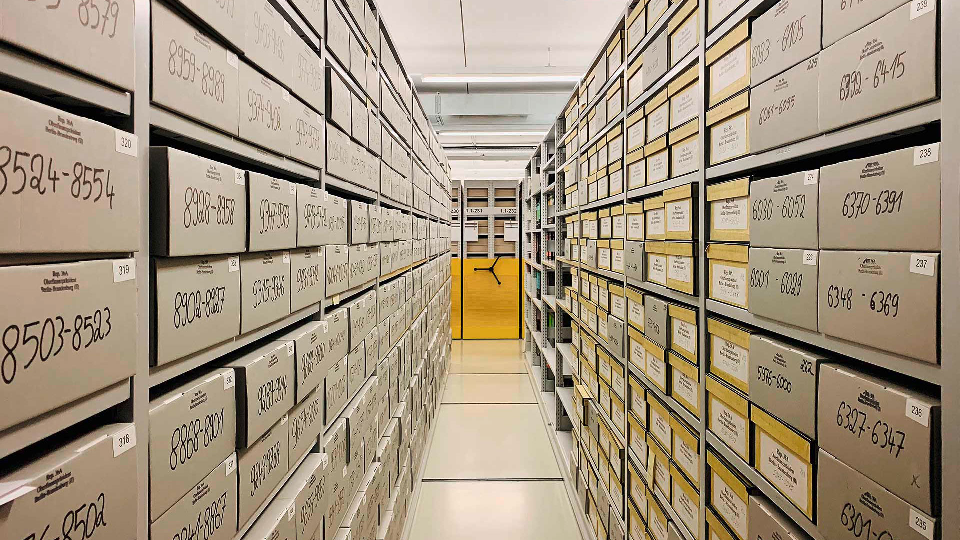 Blick in Archiv-Magazin. Enger Gang in starker Flucht mit Archivboxen links und rechts.