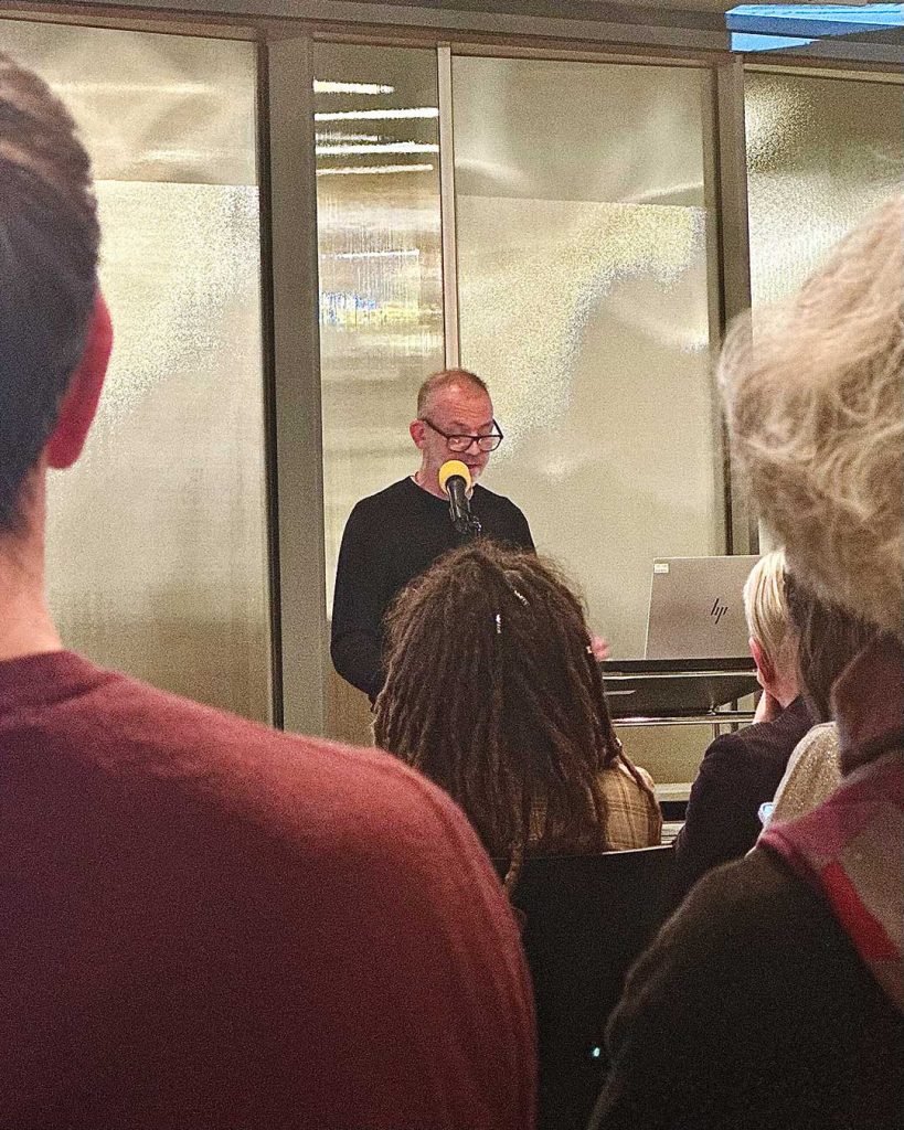 Person auf Bühne hinter Podest mit Mikrofon. Blick durch Publikum