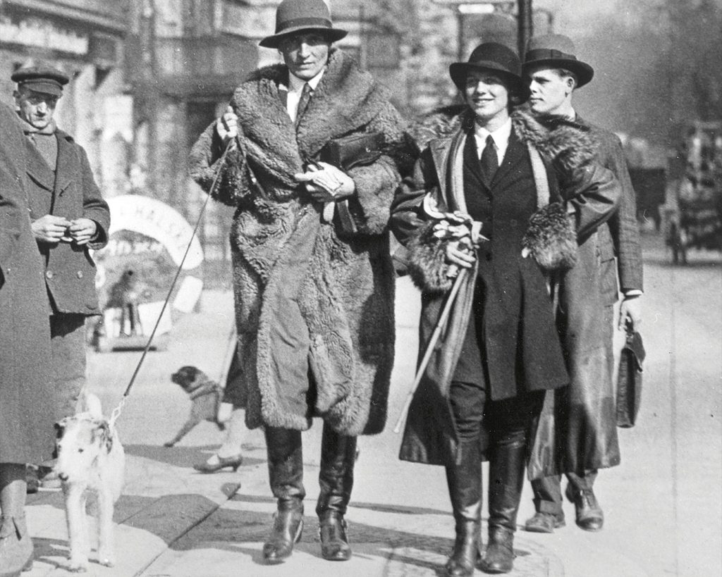 Historische Aufnahme, schwarzweiß, ca. 1920. Personen in hochwertiger Kleidung spazierung durch die Straße