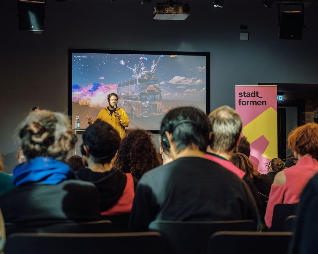 Keynote auf der Bühne der stadt_formen Konferenz. Im Vordergrund Publikum. Auf der Bühne Moderation.