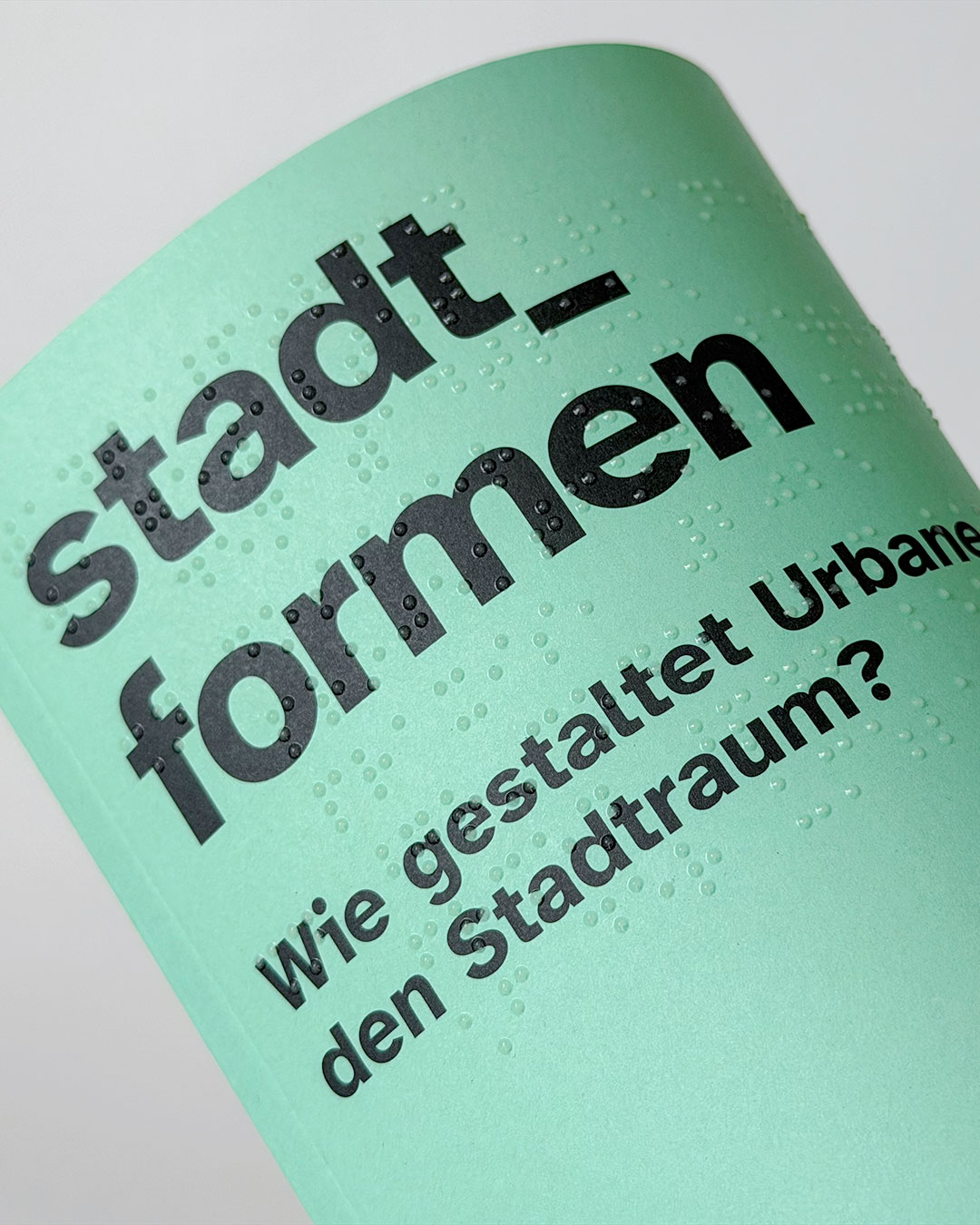 Gerollte Publikation mit Braille Druck. Titel: stadt_formen. Schwarzer Text auf mintgrünem Grund